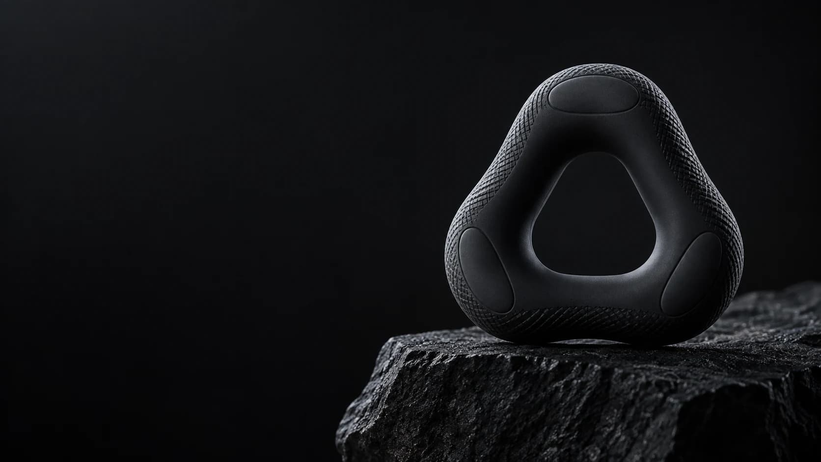 A sculptural black triangular GRIPLR grip trainer on dark stone